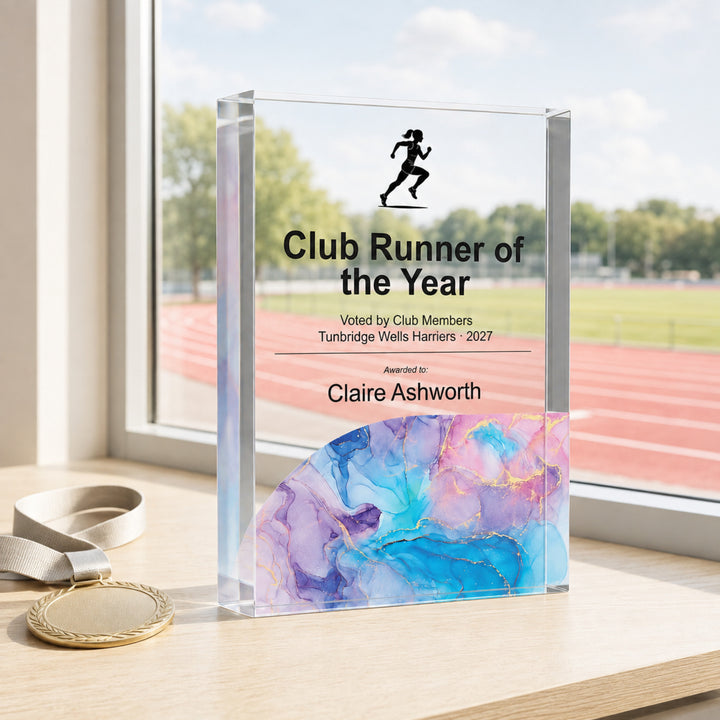 Personalised running trophy in clear acrylic printed Club Runner of the Year, beside an athletics track