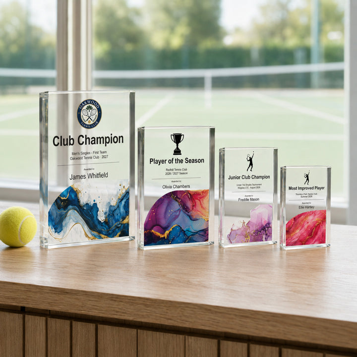 Four personalised tennis trophies in different sizes displayed side by side for a prize giving