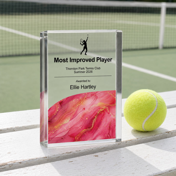 Personalised tennis trophy printed Most Improved Player with a pink base, beside a tennis ball