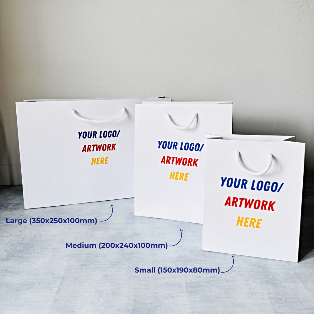 Three white paper gift bags with customisable text on a grey surface