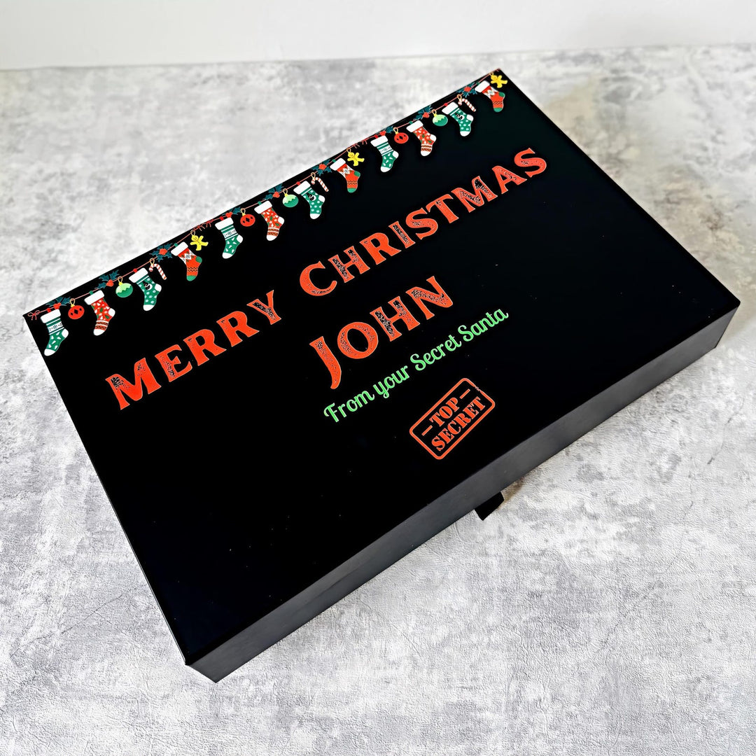 Black festive gift box with 'Merry Christmas John' text and festive design on a gray surface