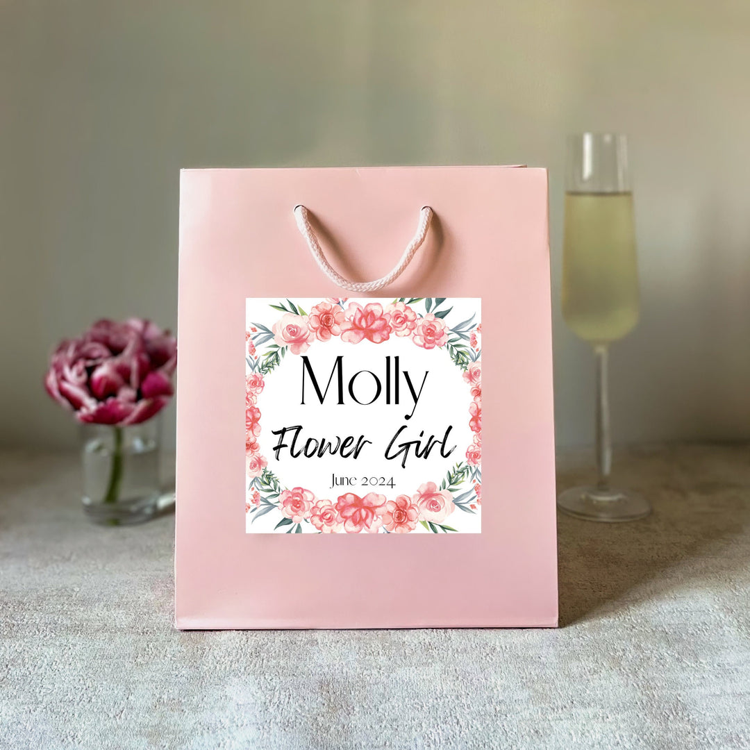 A pink gift bag with a personalised hen party gift bag floral sticker label featuring the name 'Molly' and the title 'Flower Girl' for a hen party.
