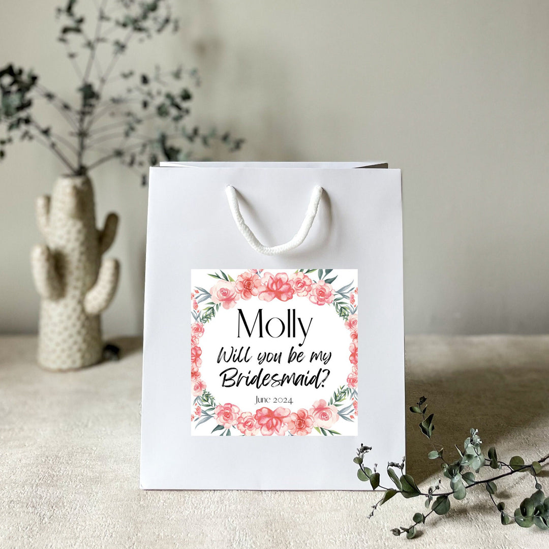 A white gift bag with a personalised hen party gift bag floral sticker label featuring the name 'Molly' and the title 'Flower Girl' for a hen party.
