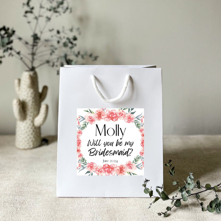A white gift bag with a personalised hen party gift bag floral sticker label featuring the name 'Molly' and the title 'Flower Girl' for a hen party.