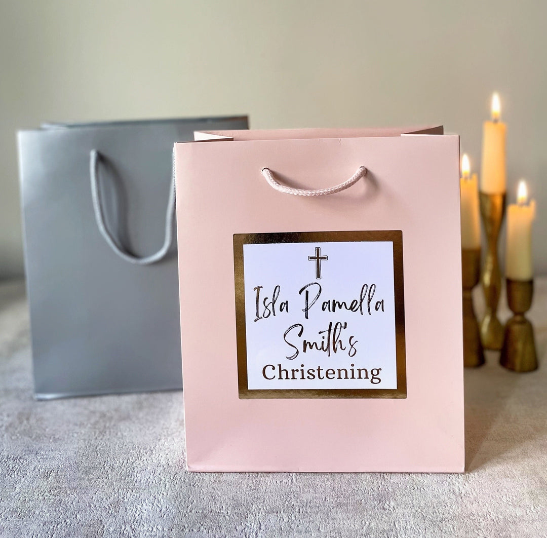 Personalised Christening gift bags with custom foil stickers, one in pink and the other in silver, with text personalisation visible on the pink bag.