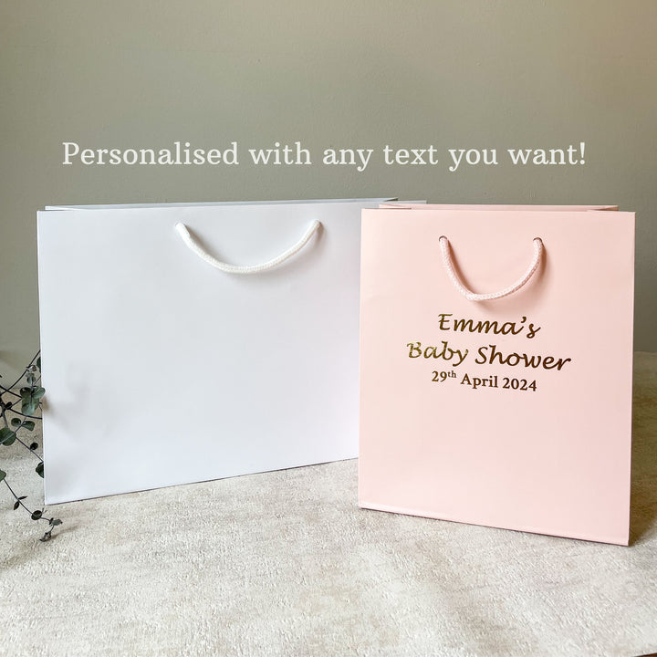 white and pink hen party gift bag with gold text and detailing, displayed next to a glass of champagne and decorative foliage.