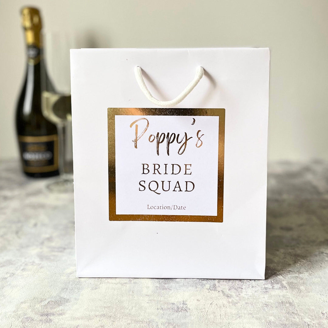 Luxury Personalised Bride Squad White Gift Bag and white sticker with gold foil writing and sticker. The Sticker writing says Bride Squad. Perfect for hen party favours and hen party gift bags for your bride tribe on your hen do and bridesmaid gifts.