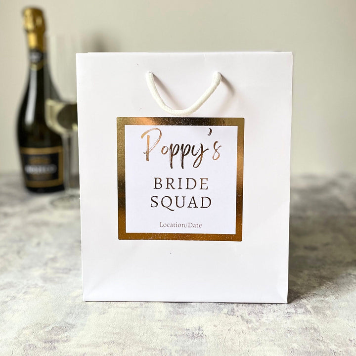 Luxury Personalised Bride Squad White Gift Bag and white sticker with gold foil writing and sticker. The Sticker writing says Bride Squad. Perfect for hen party favours and hen party gift bags for your bride tribe on your hen do and bridesmaid gifts.